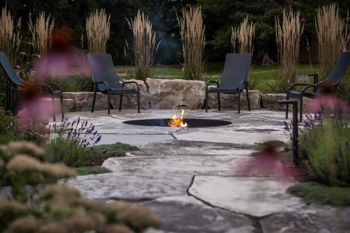 Natural flagstone fire pit patio with seating area surrounded by ornamental grasses and gardens in Strathroy Ontario