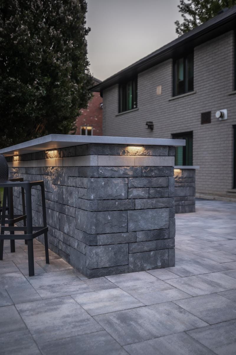 Custom outdoor kitchen and bar with concrete block construction and integrated lighting on a paver patio in Hyde Park London Ontario